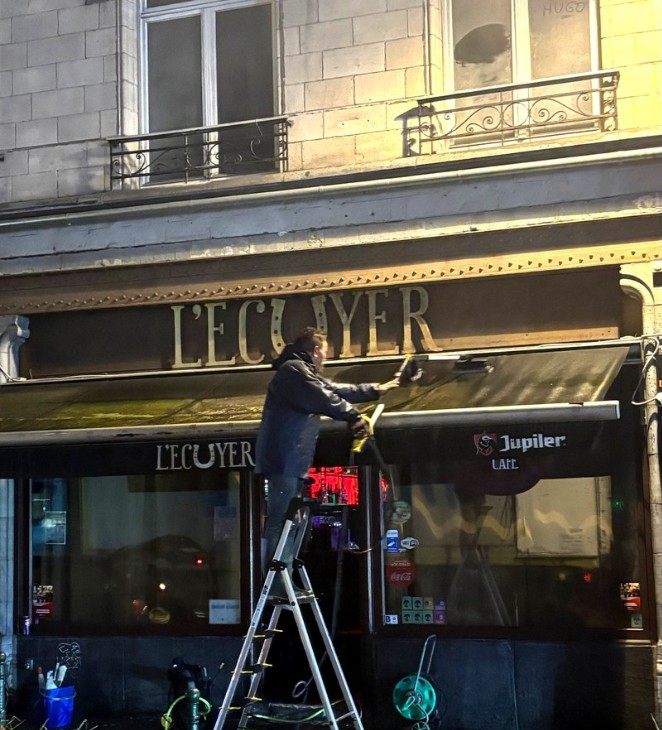 Agent JM Group sur une échelle pendant le nettoyage de bâches d'un bar